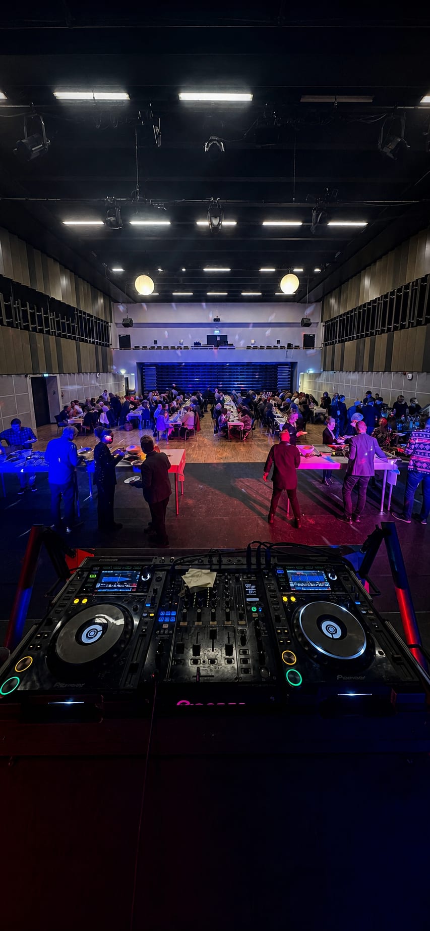 DJ decks in foreground overlooking a hall with guests seated at tables before a party