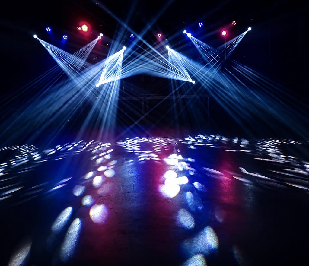Stage light show with crisscrossing blue beams and colorful spotlight patterns on floor