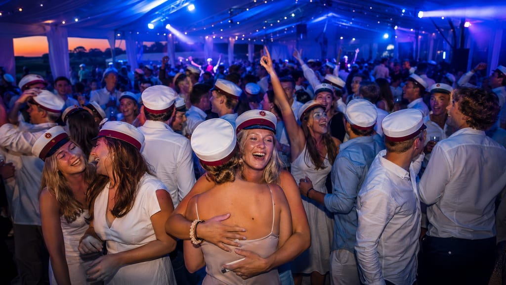 Crowd of graduates in white sailor caps dancing at a festive tent party at dusk